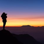 woman standing on a mountain peak looking at the sunrise, symbolizing life purpose