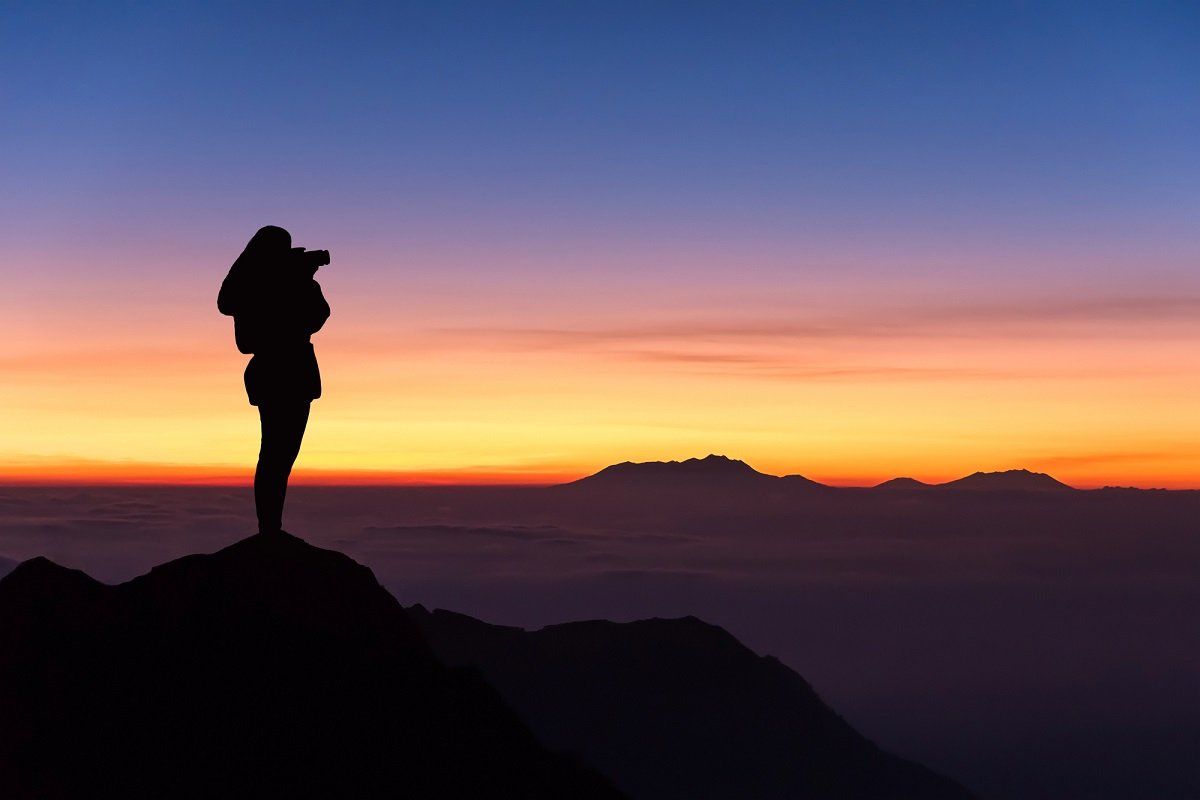 woman standing on a mountain peak looking at the sunrise, symbolizing life purpose