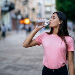 A woman drinking water while looking at a water bottle, representing the journey to proper hydration