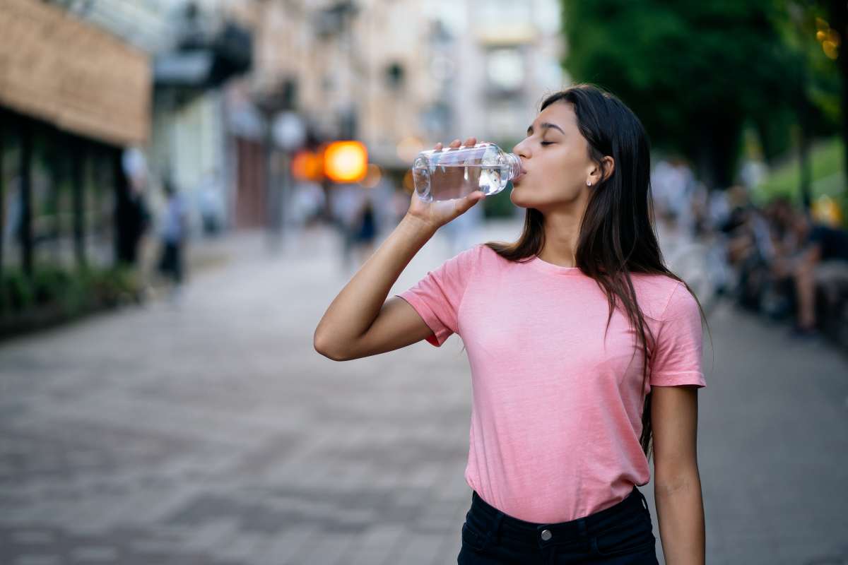 A woman drinking water while looking at a water bottle, representing the journey to proper hydration