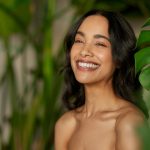 young woman touching her glowing skin and smiling, symbolizing healthy aging