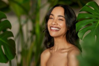 young woman touching her glowing skin and smiling, symbolizing healthy aging