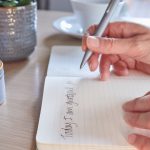 A person writing in a beautiful gratitude journal with a cup of coffee, representing the practice of gratitude and mindfulness